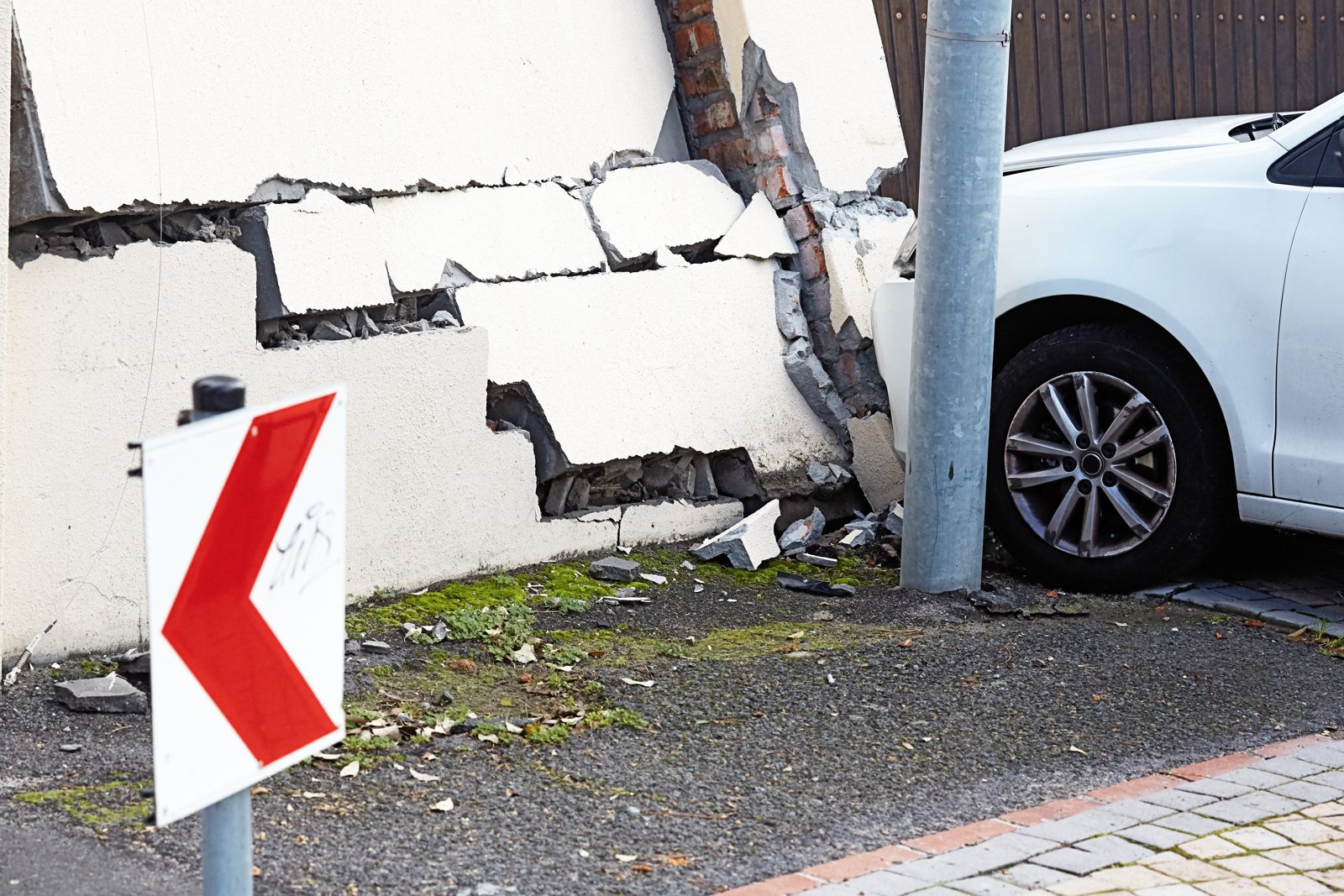Car crashed into a building wall with cracked stucco and a bent sign