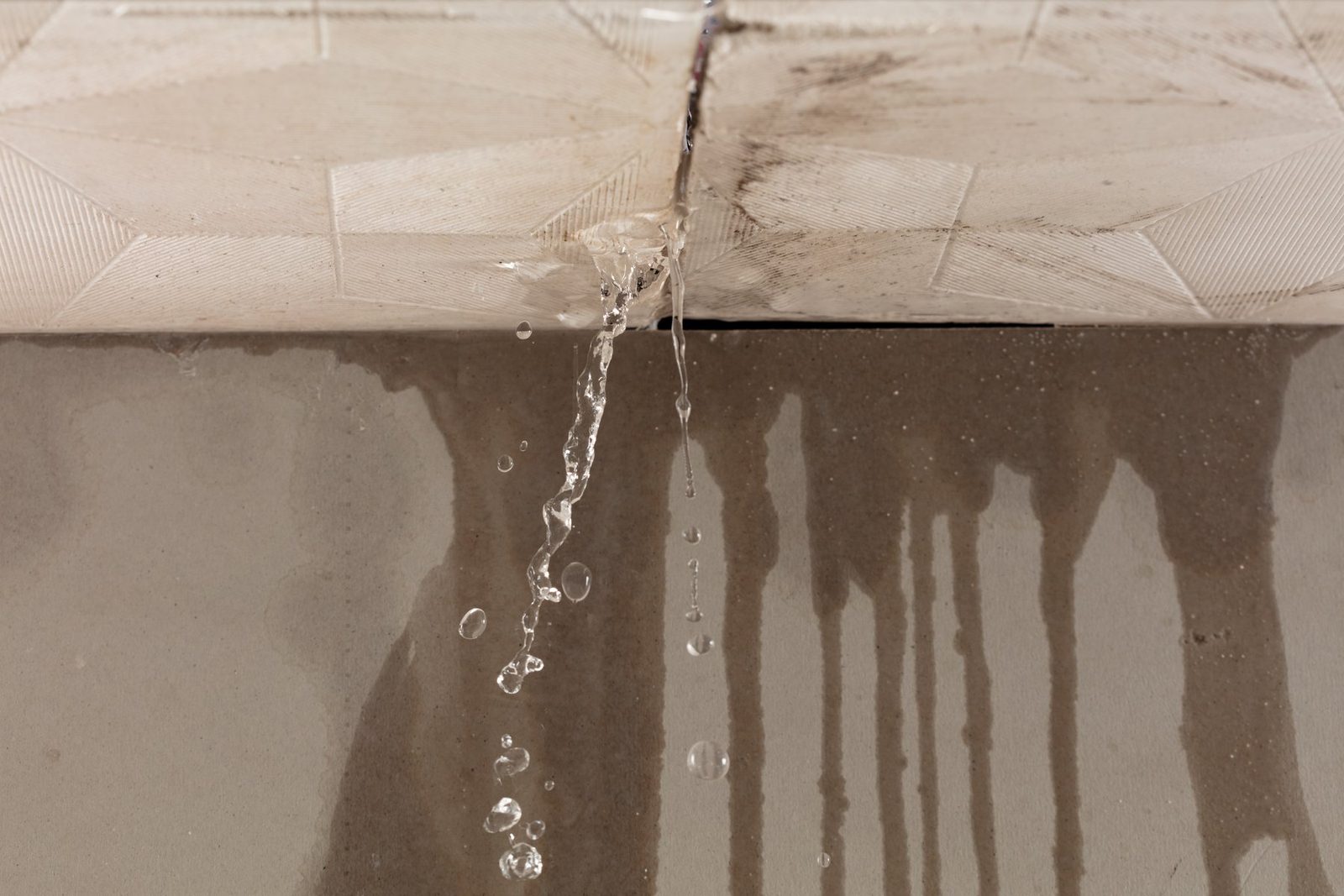 Water dripping from a ceiling seam and streaking down a wall
