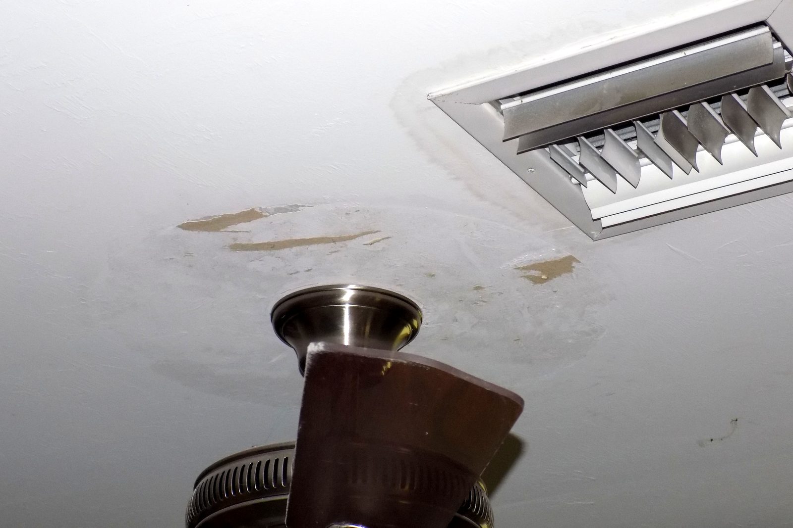 Water stains on a ceiling around an air conditioning vent and a ceiling fan