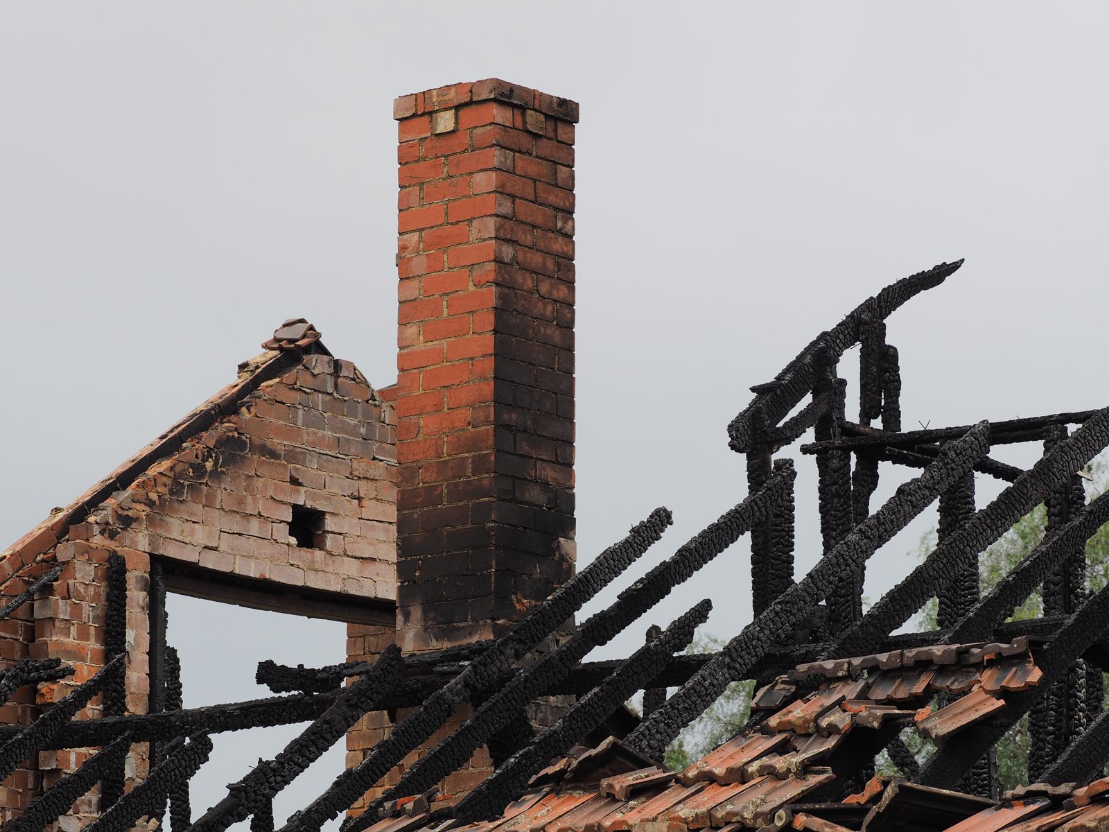 Brick chimney standing over charred roof rafters after a chimney fire