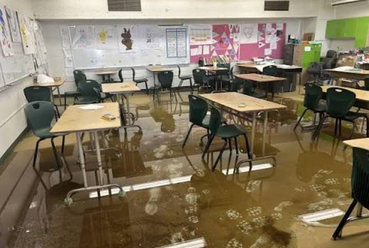 Flooded classroom with standing water covering the floor between desks