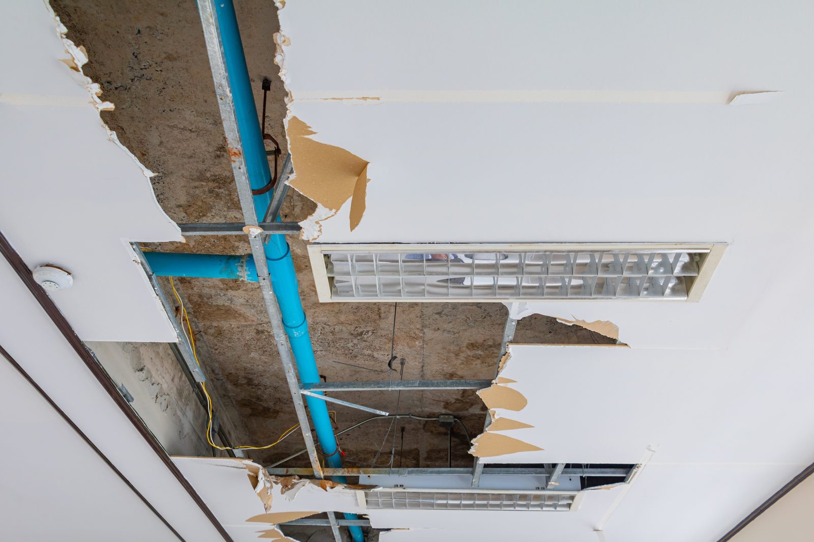 Collapsed commercial ceiling tiles with exposed water-damaged drywall and a burst pipe
