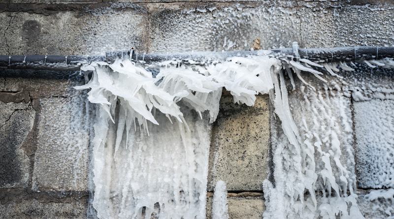 Heavy ice buildup on a frozen exterior pipe at a condo or HOA association building