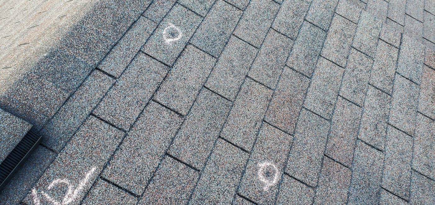 Hail bruises circled in chalk on asphalt shingles during a roof test square
