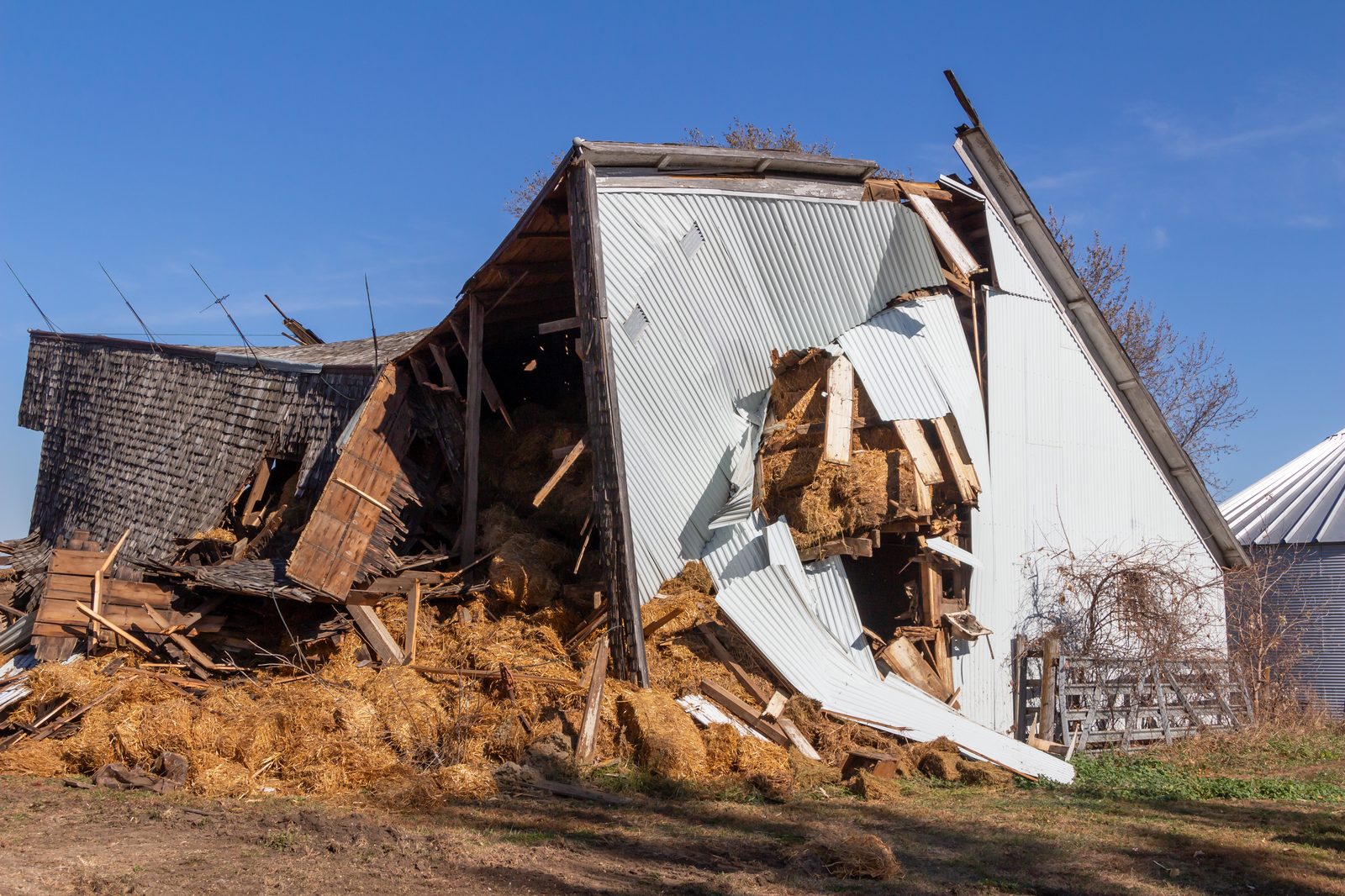 Wood-frame farm building torn open by tornado winds, interior exposed