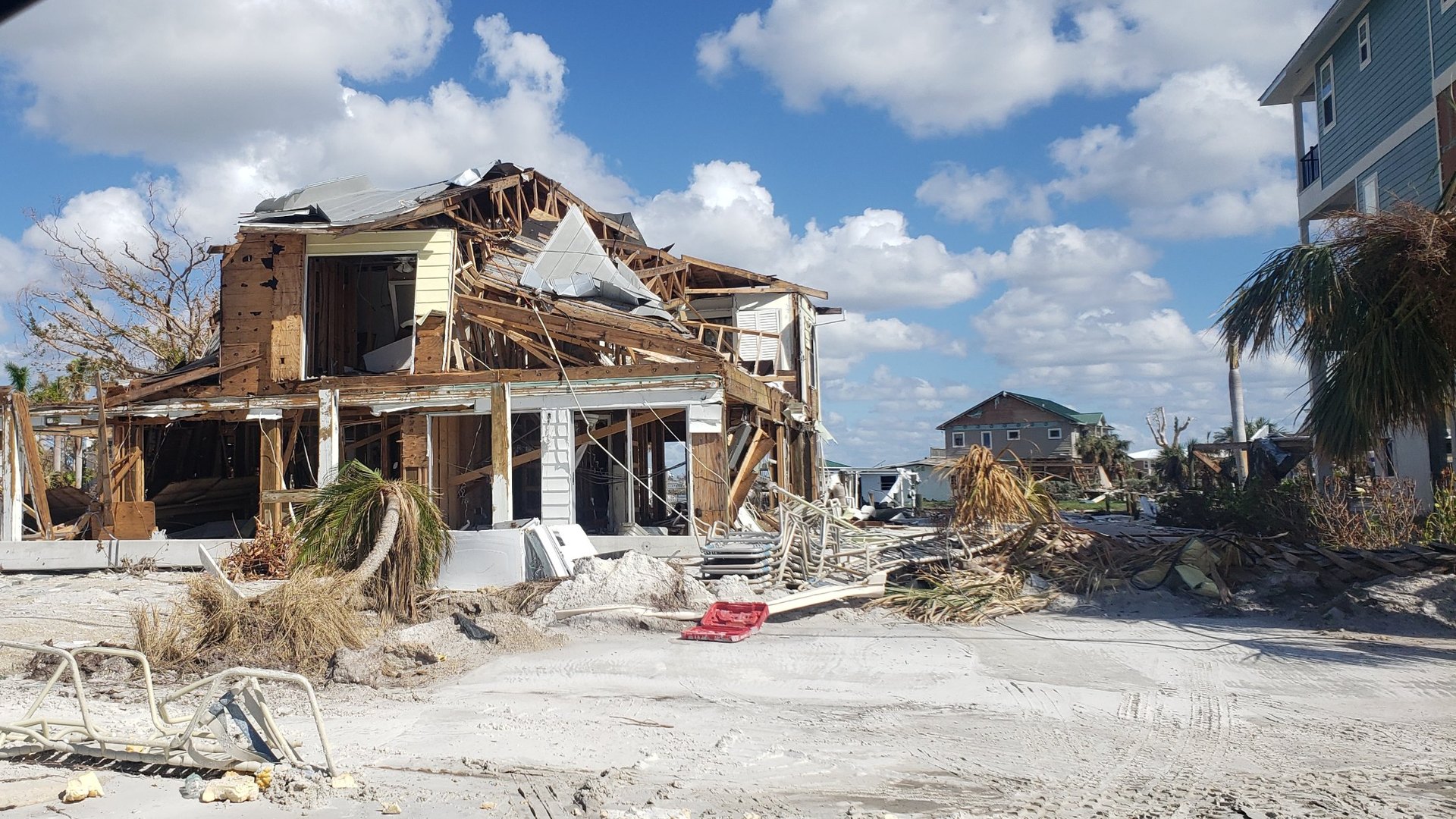 Beach house torn open by a hurricane, with debris and sand covering the street in a Florida coastal neighborhood