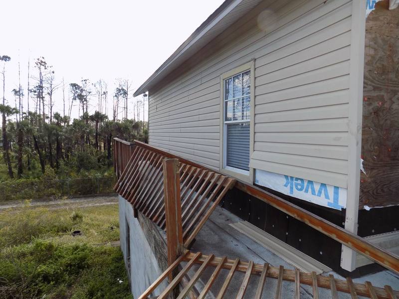 Damaged deck railing and torn siding exposing house wrap after hurricane wind