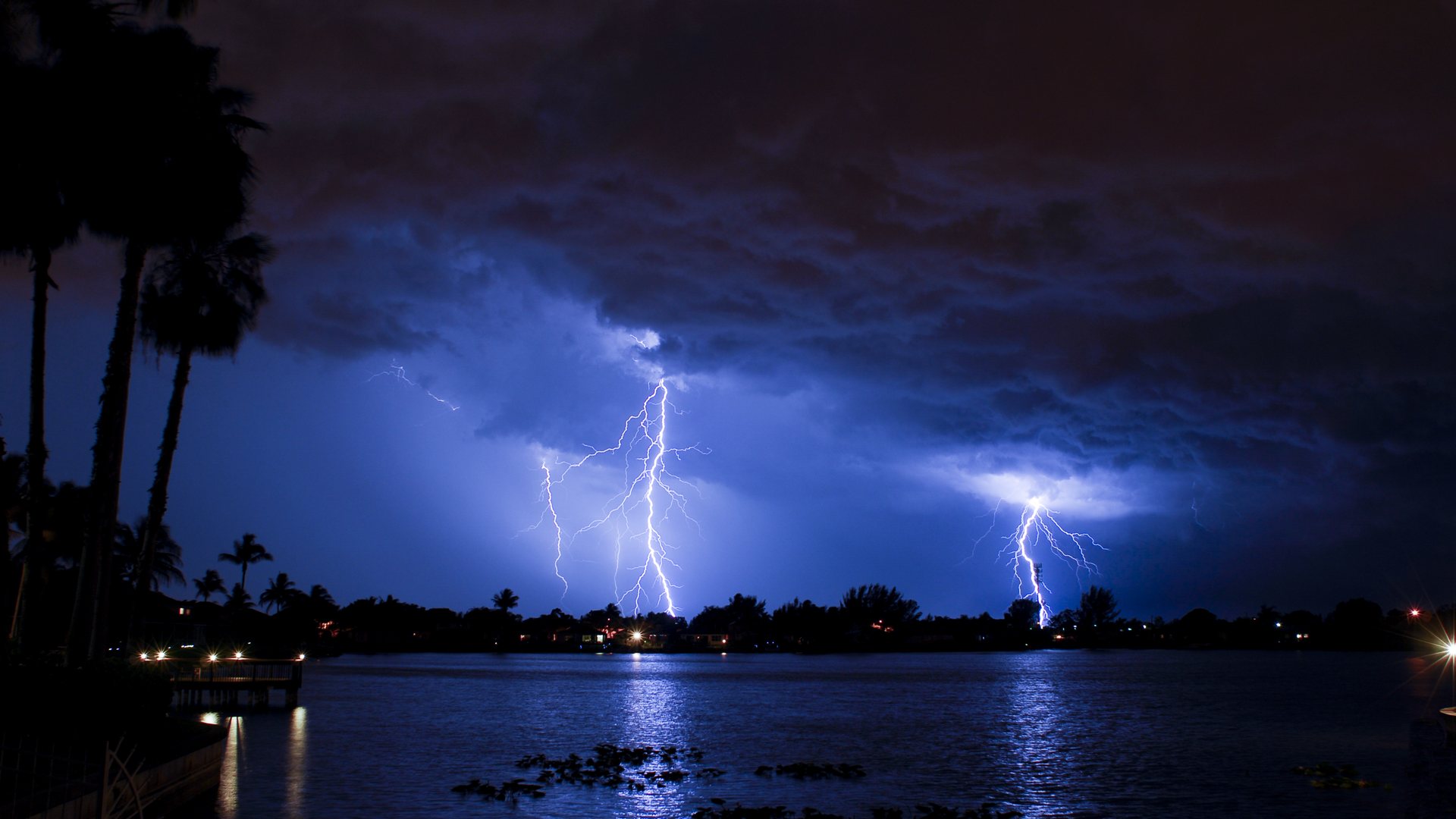 Relámpagos sobre un lago con casas y palmeras de noche