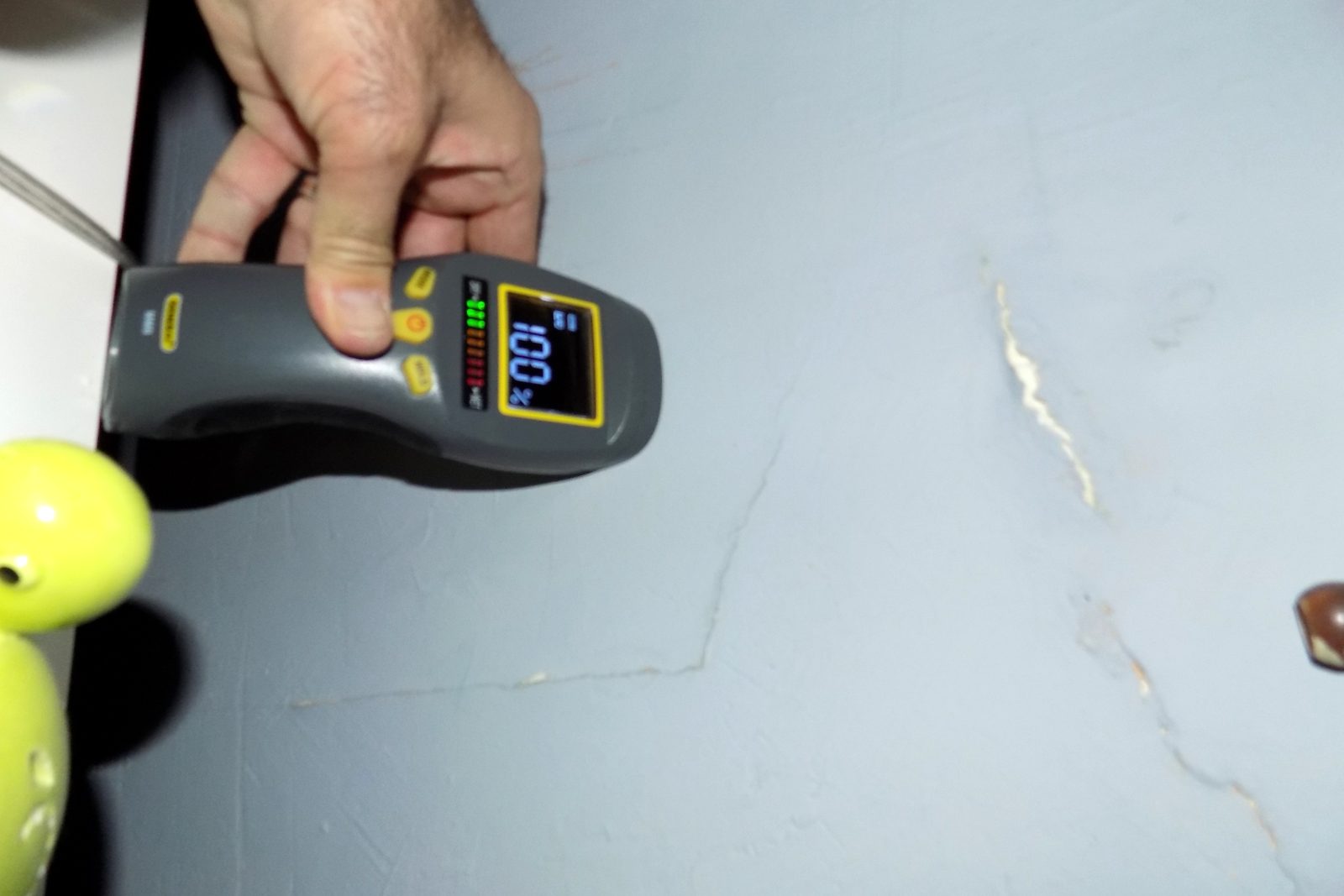 Moisture meter showing a 100% reading next to a crack in a floor