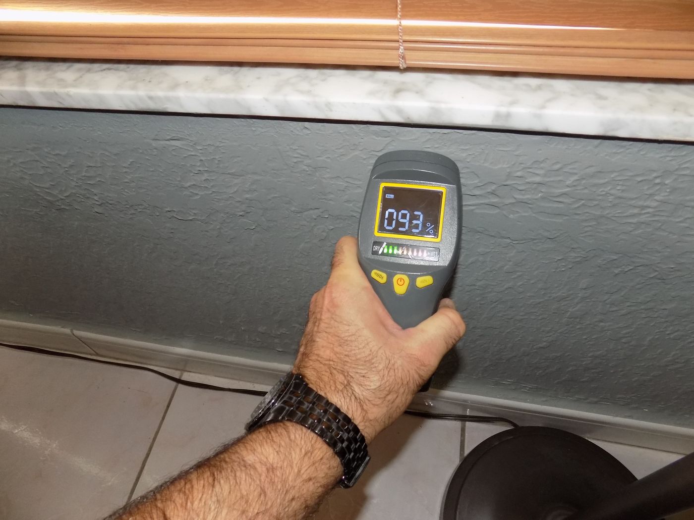Medidor de humedad que marca 93% en una pared junto al zócalo