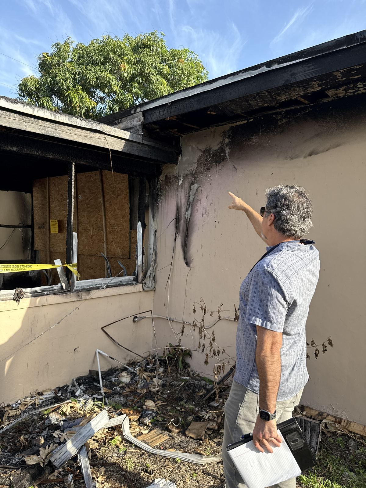 Ajustador público señalando daños por incendio en la pared exterior de una casa