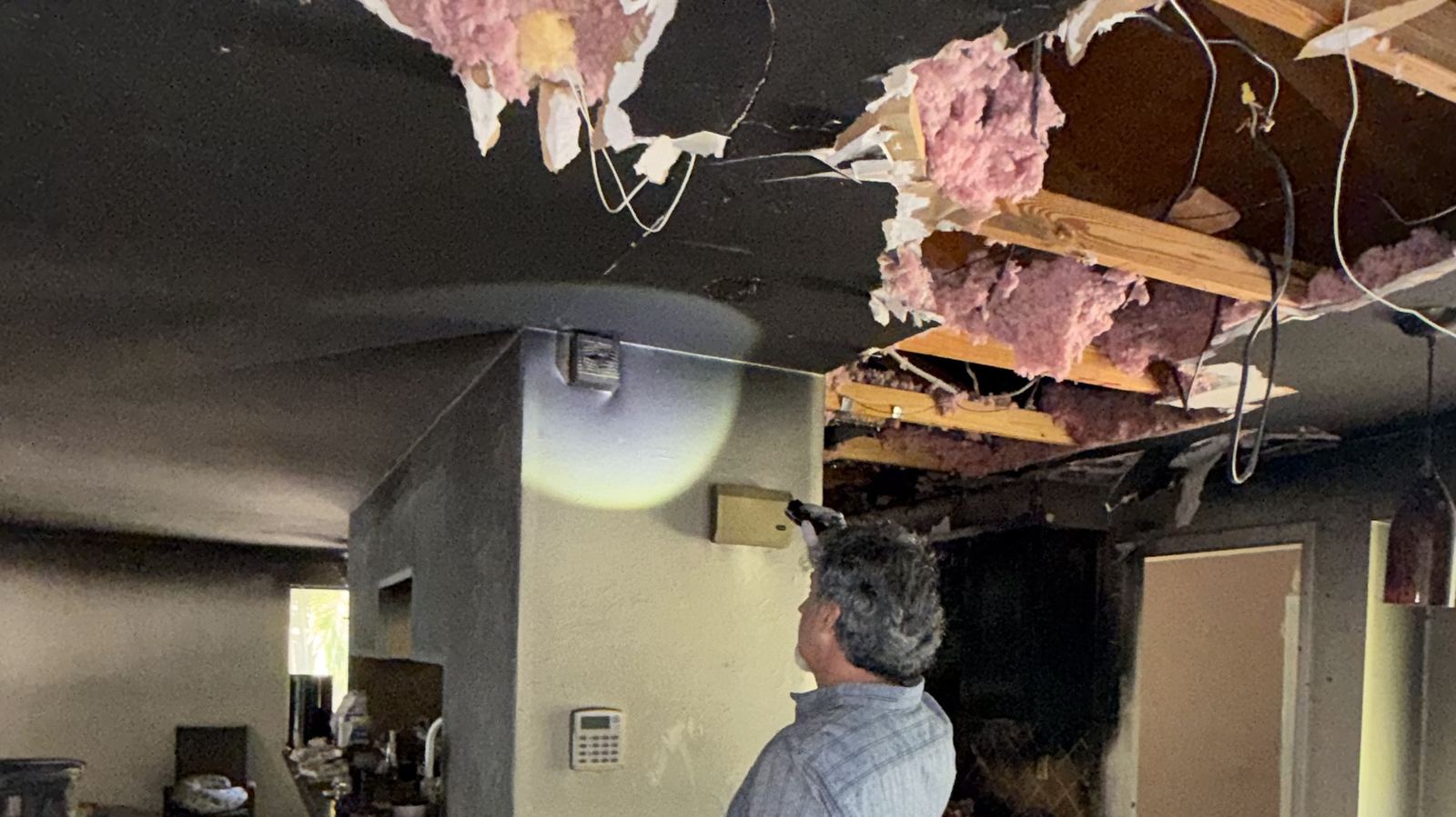 Public adjuster with a clipboard inspecting a fire-damaged room, burned ceiling joists and charred insulation overhead