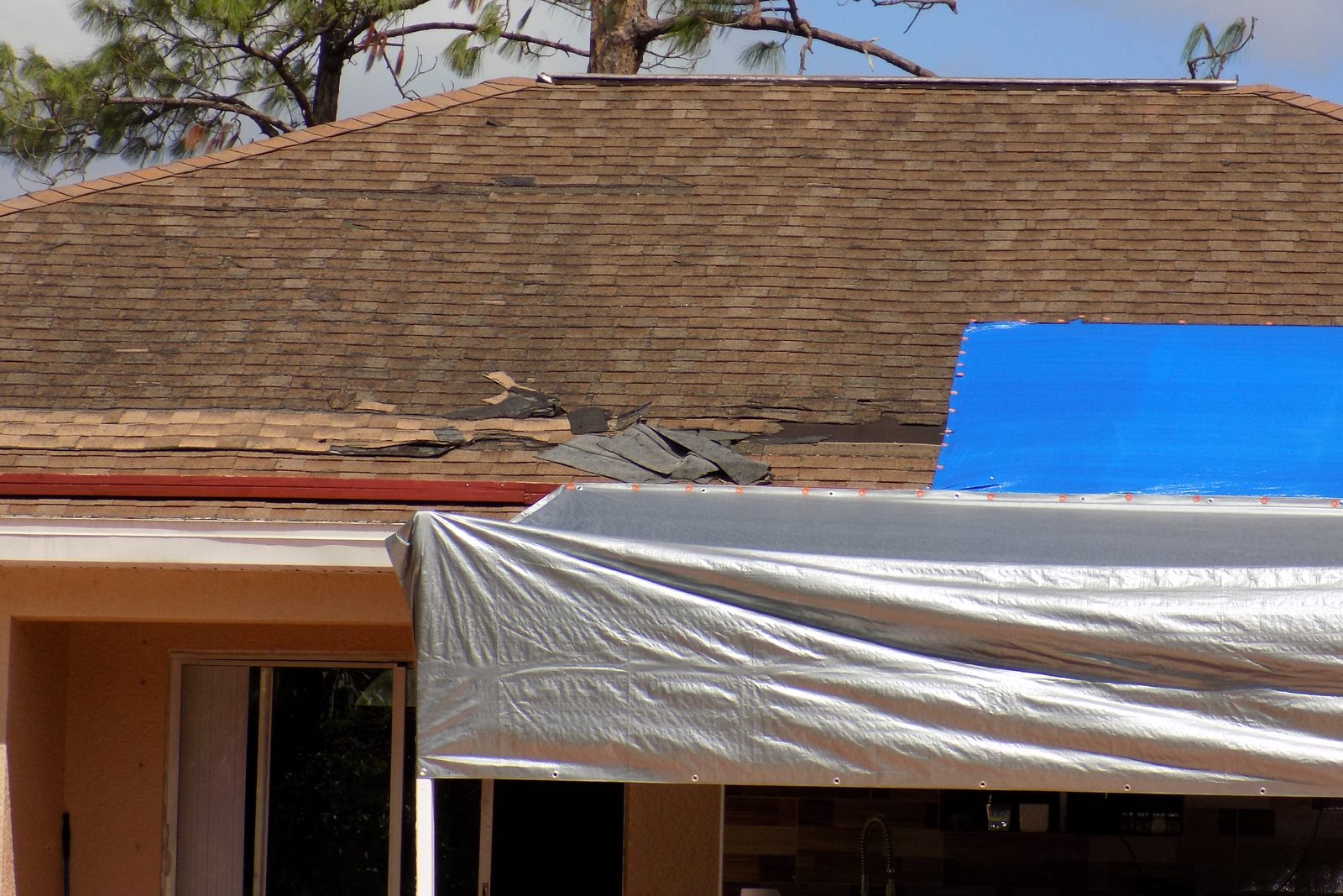 Shingle roof with a blue tarp and a temporary cover over storm damage