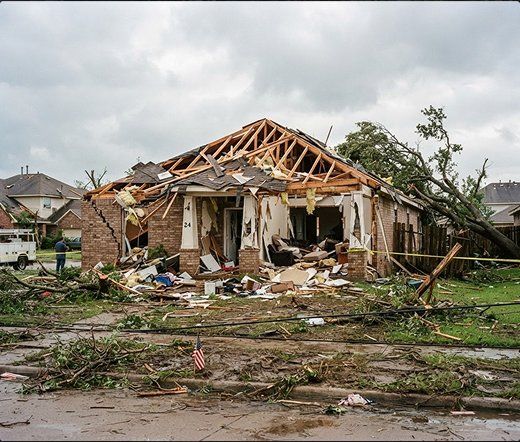 House with its roof and walls collapsed after a tornado, debris scattered across the yard