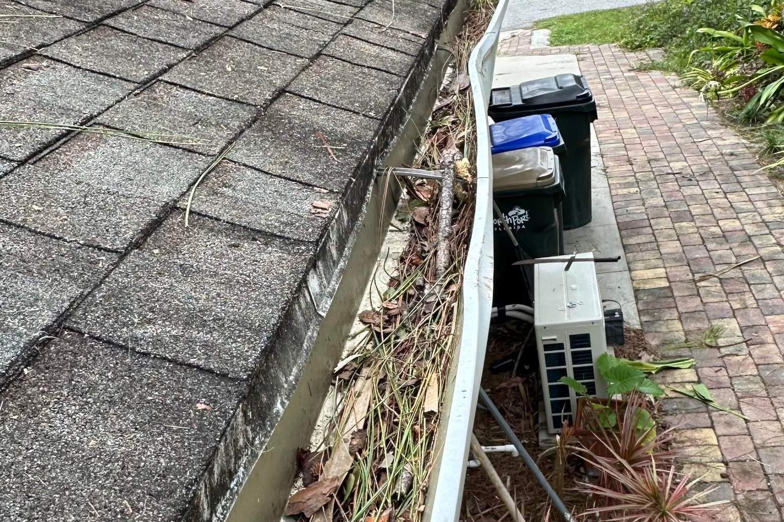 Storm debris on an aging shingle roof with a bent gutter after a hurricane, the kind of roof insurers sometimes deny as wear and tear