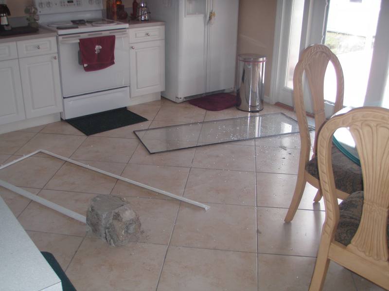 Shattered glass and the brick used to break in scattered across a kitchen floor