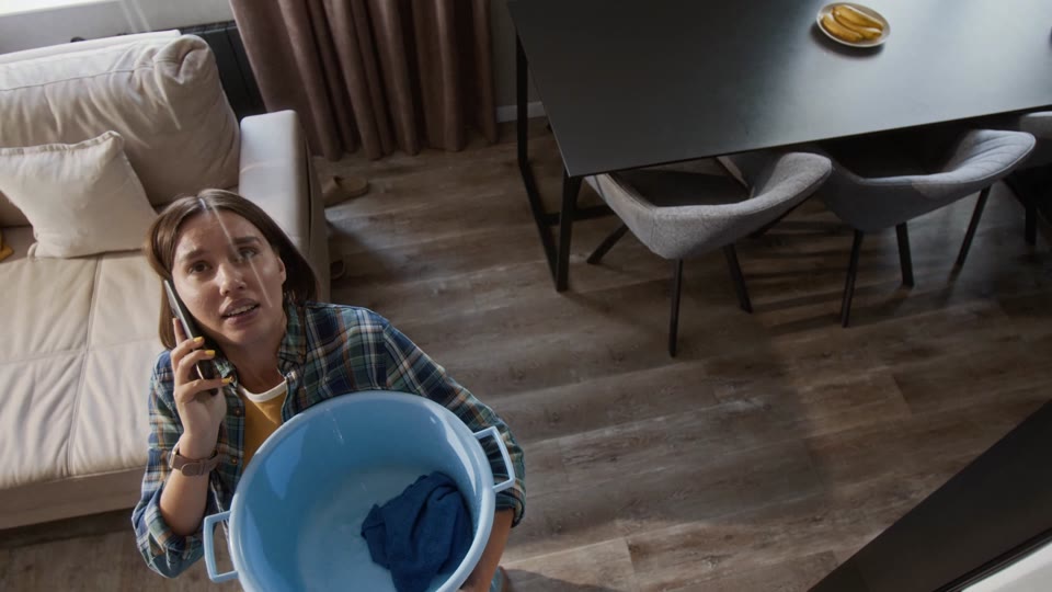 Woman on the phone holding a bucket of water during a leak in her apartment
