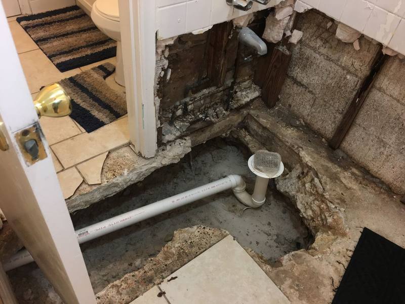 Bathroom floor removed down to the subfloor during a water damage repair, with exposed plumbing