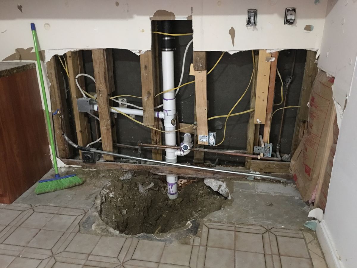 Kitchen cabinets removed to expose water-damaged plumbing and wall in a Southeast Florida home