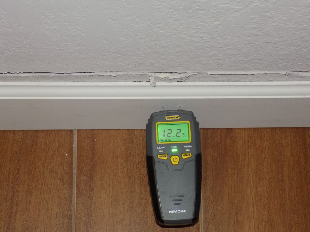 Moisture meter reading elevated wood moisture at a cracked wall during a water damage inspection in Camden, NJ