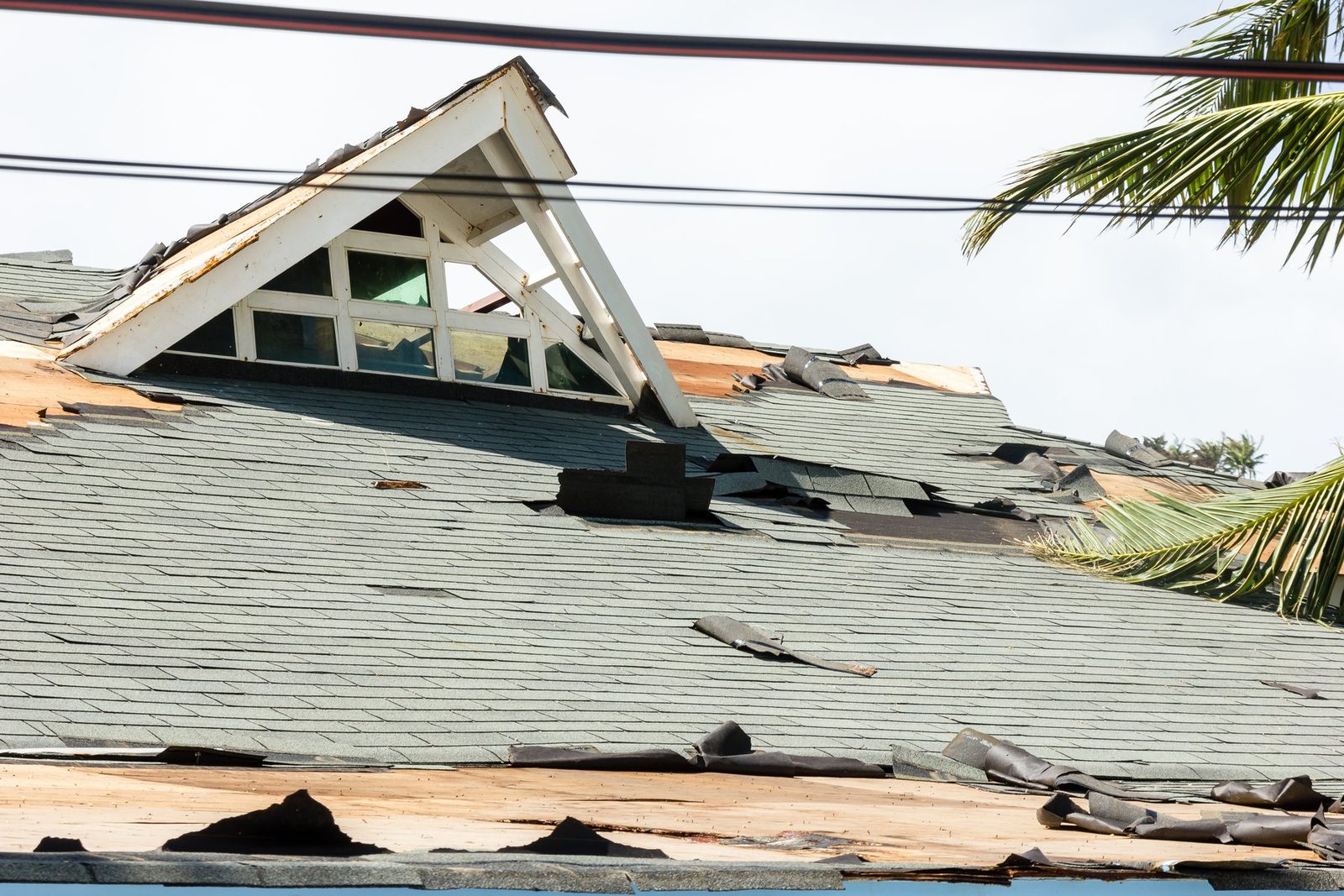 Hurricane wind damage to an asphalt shingle roof with shingles torn away near a dormer