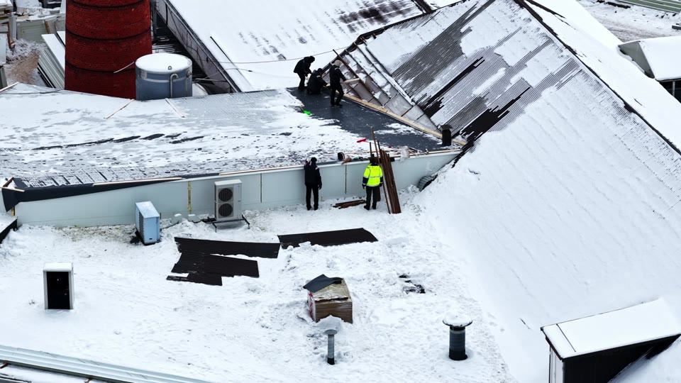Repair crew clearing snow and ice from a commercial roof after a winter storm