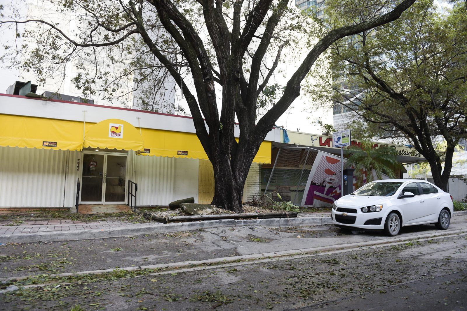 Yellow commercial building with storm debris and a fallen tree in the parking lot